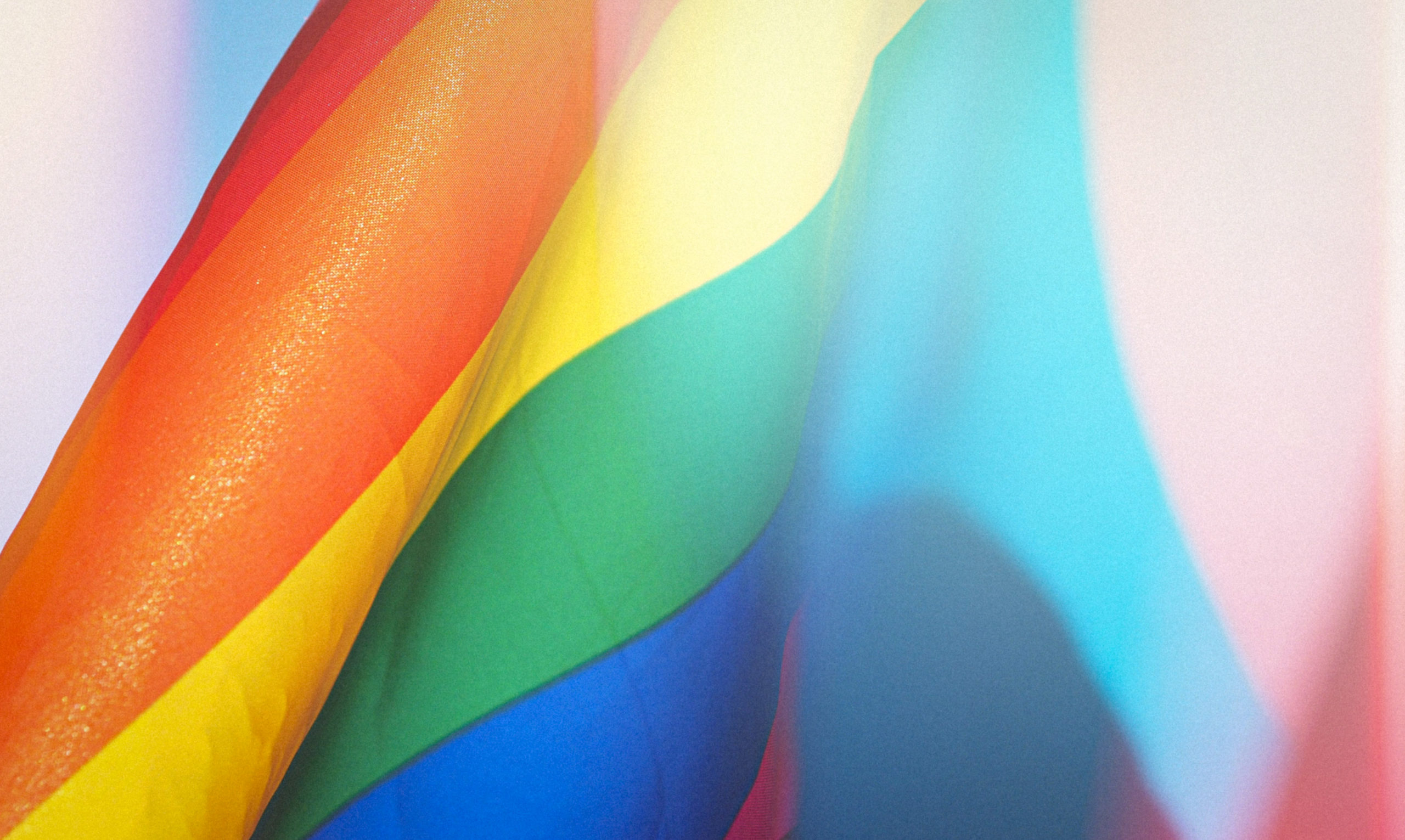 A pride and trans flag against a blue sky.